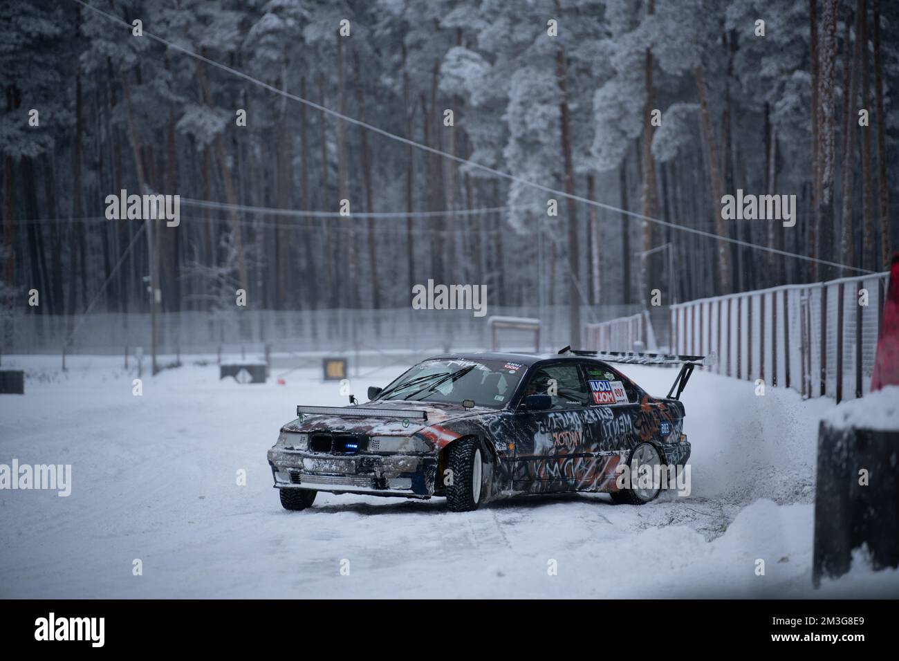 12-12-2022 Riga, Lettland ein Auto, das im Schnee neben einem Zaun und Bäumen im Hintergrund geparkt ist. . Stockfoto