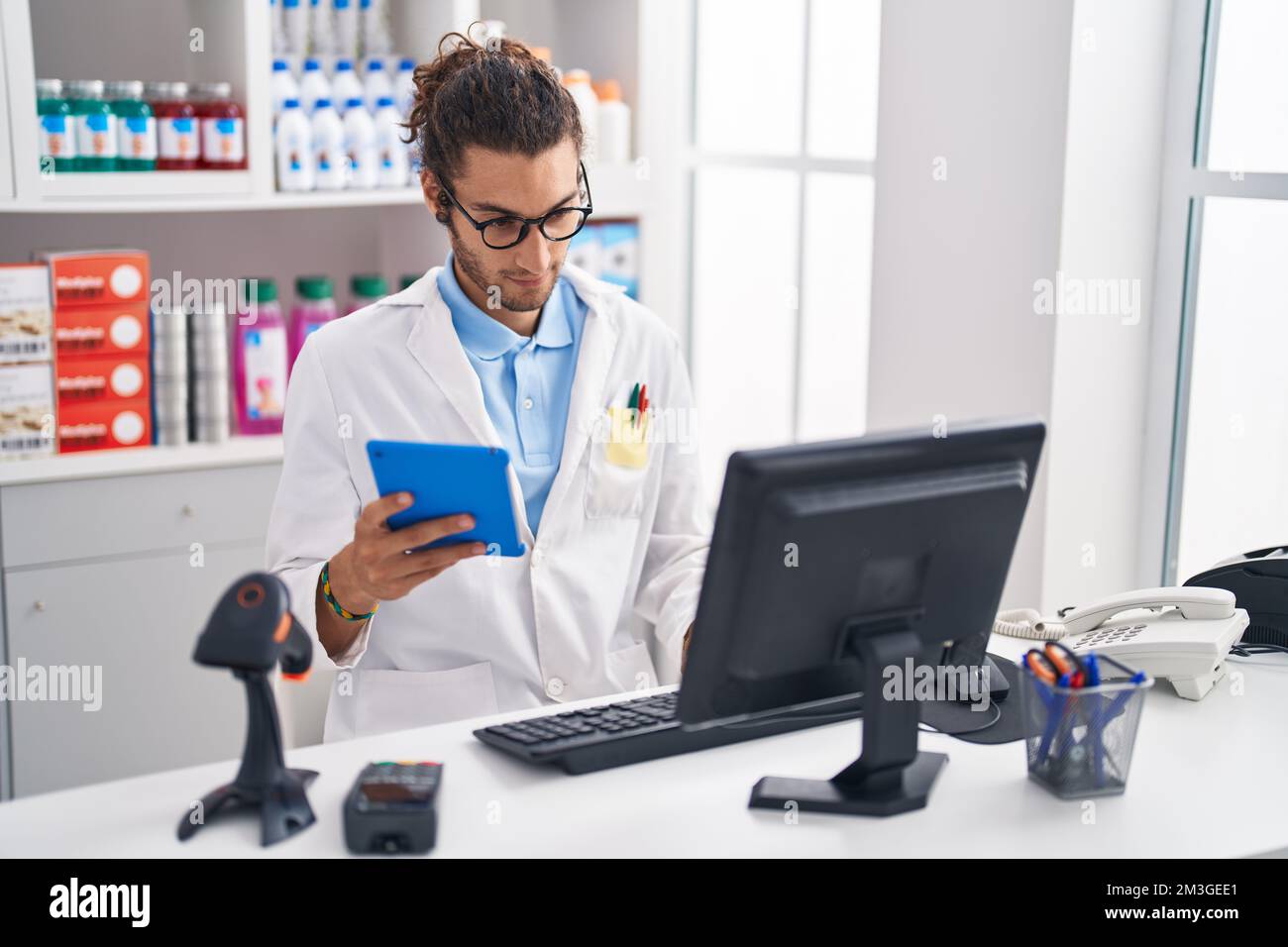 Junger hispanischer Apotheker mit Touchpad und Computer, der in der Apotheke arbeitet Stockfoto
