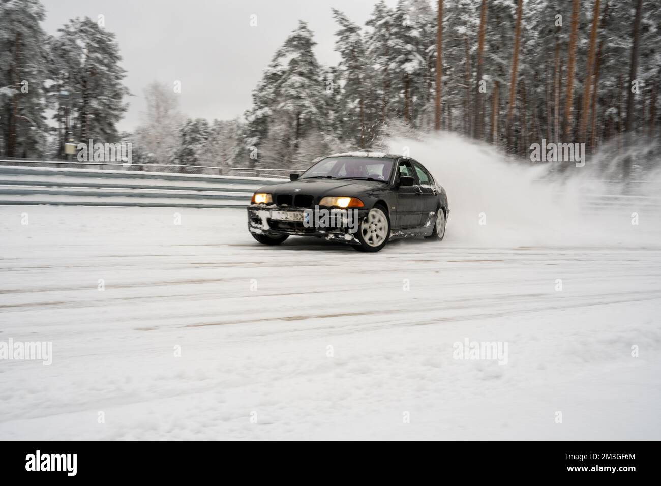 12-12-2022 Riga, Lettland ein Auto, das auf einer verschneiten Straße mit Bäumen im Hintergrund fährt und dahinter Schnee in die Luft jagt. . Stockfoto