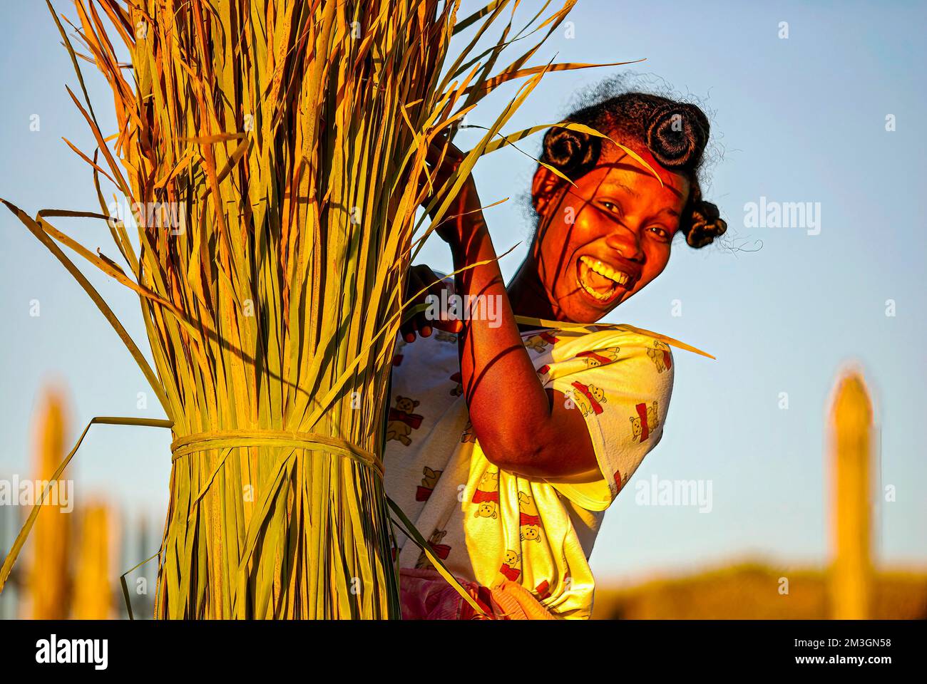 Frau lacht hinter einem Strohballen nach der Ernte, Mankara, Madgaskar * Mädchen lächelt nach der Ernte hinter einem Strohballen, Mankara Stockfoto