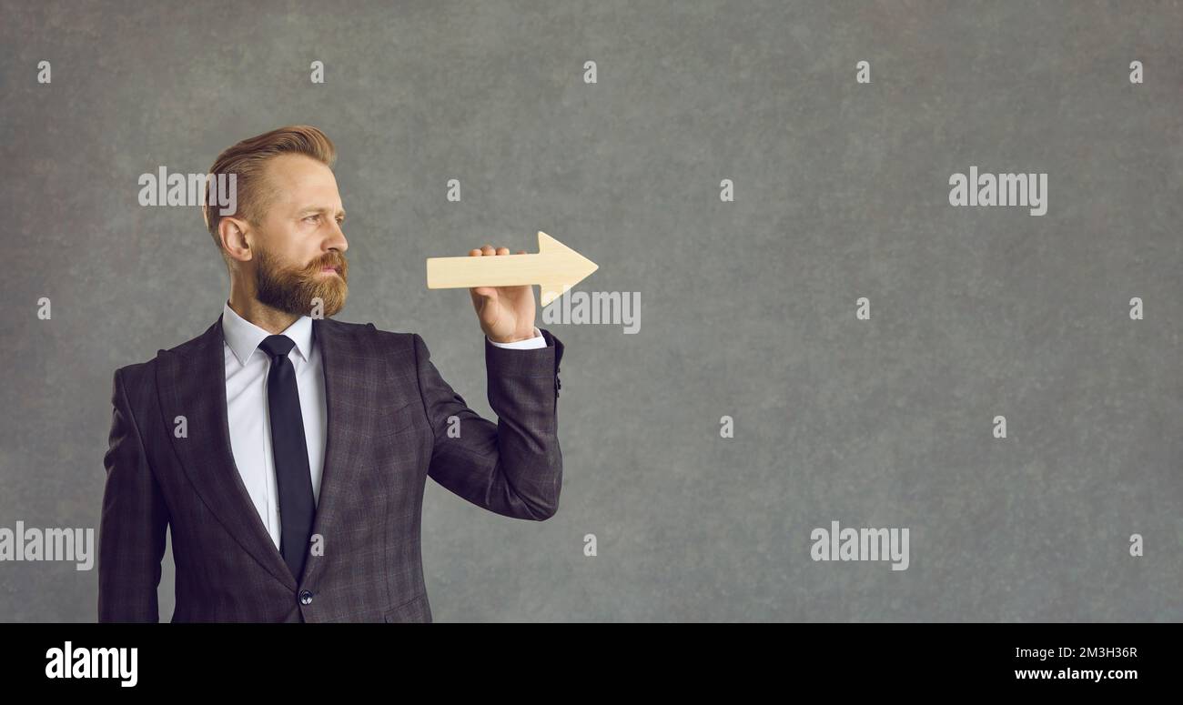 Ein seriöser Geschäftsmann, der Pfeil hält und gerade auf grauen Hintergrund blickt Stockfoto