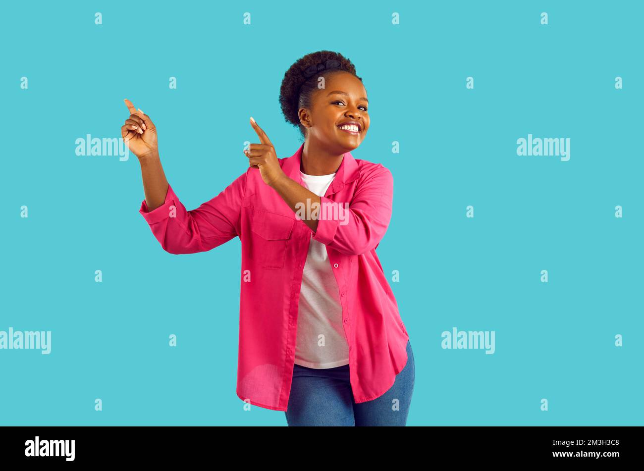 Fröhliche, fröhliche afroamerikanische Frau tanzt und zeigt auf den Kopierbereich auf türkisfarbenem Hintergrund. Stockfoto