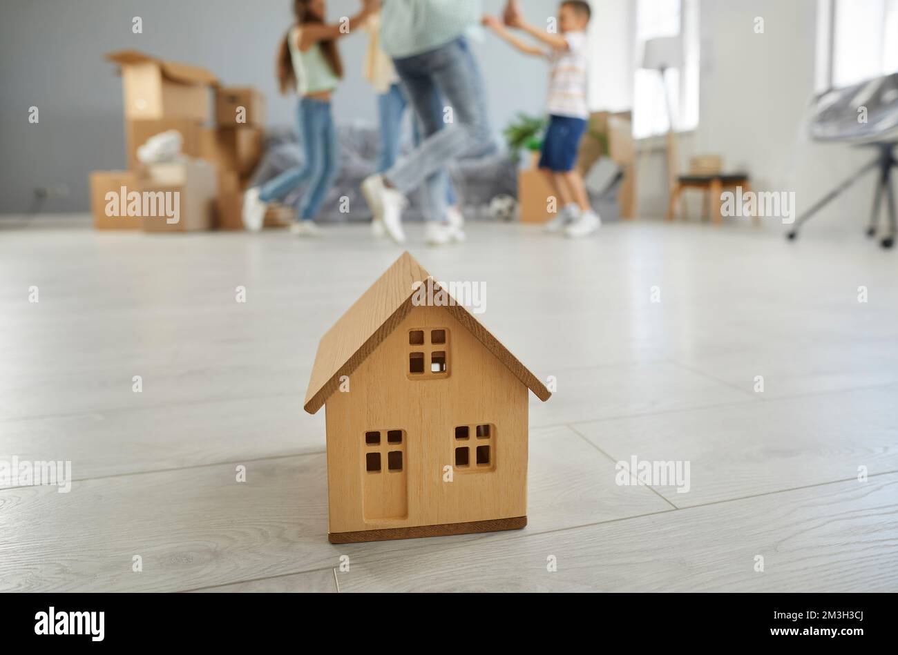 Kleines Modell eines Holzhauses auf dem Boden im Wohnzimmer im Hintergrund einer Familie, die sich gerne bewegt. Stockfoto