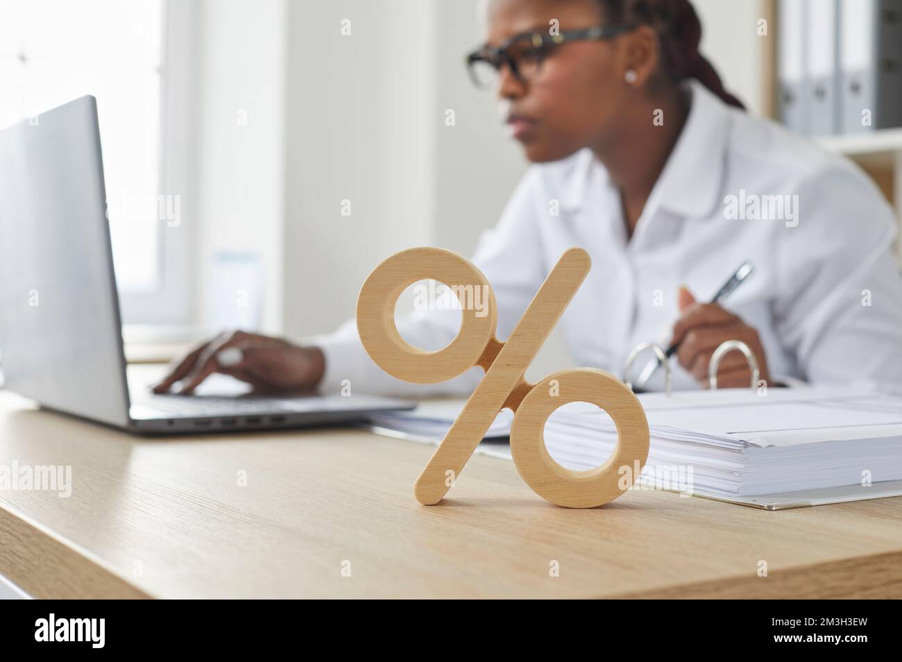 Prozentangabe am Schreibtisch, Geschäftsfrau arbeitet im Hintergrund an einem Notebook Stockfoto