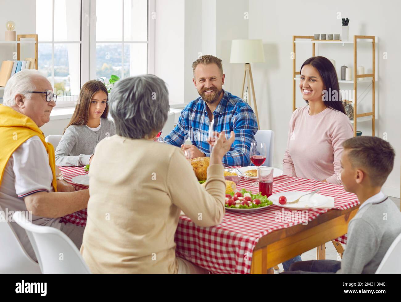 Große Familieneltern, Großeltern und Kinder unterhalten sich zu Mittag und sitzen zu Hause am Tisch. Stockfoto