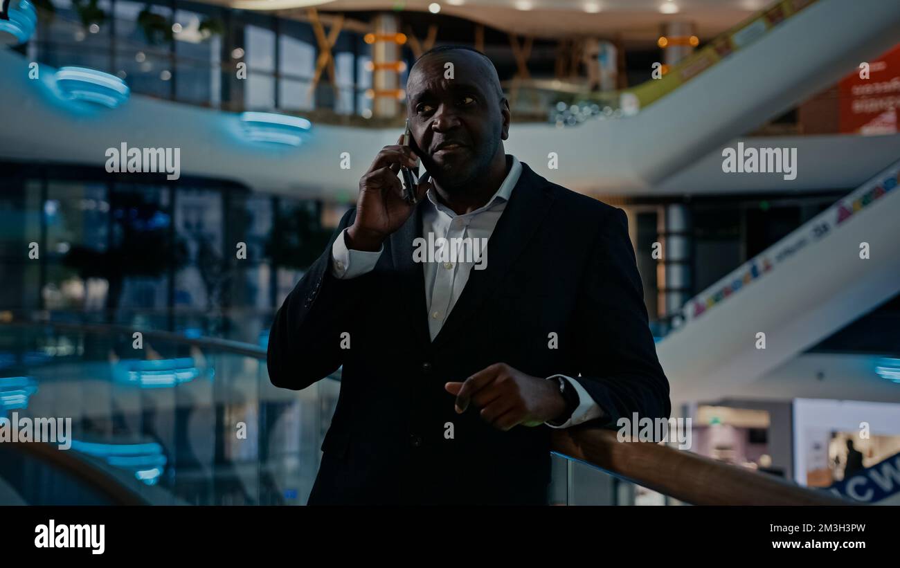 50s Beratermann telefoniert Kollegen Geschäftspartner spricht mit Smartphone im Innenbereich im Büro und zeigt die Richtung an und erklärt es. Afrikaner Stockfoto