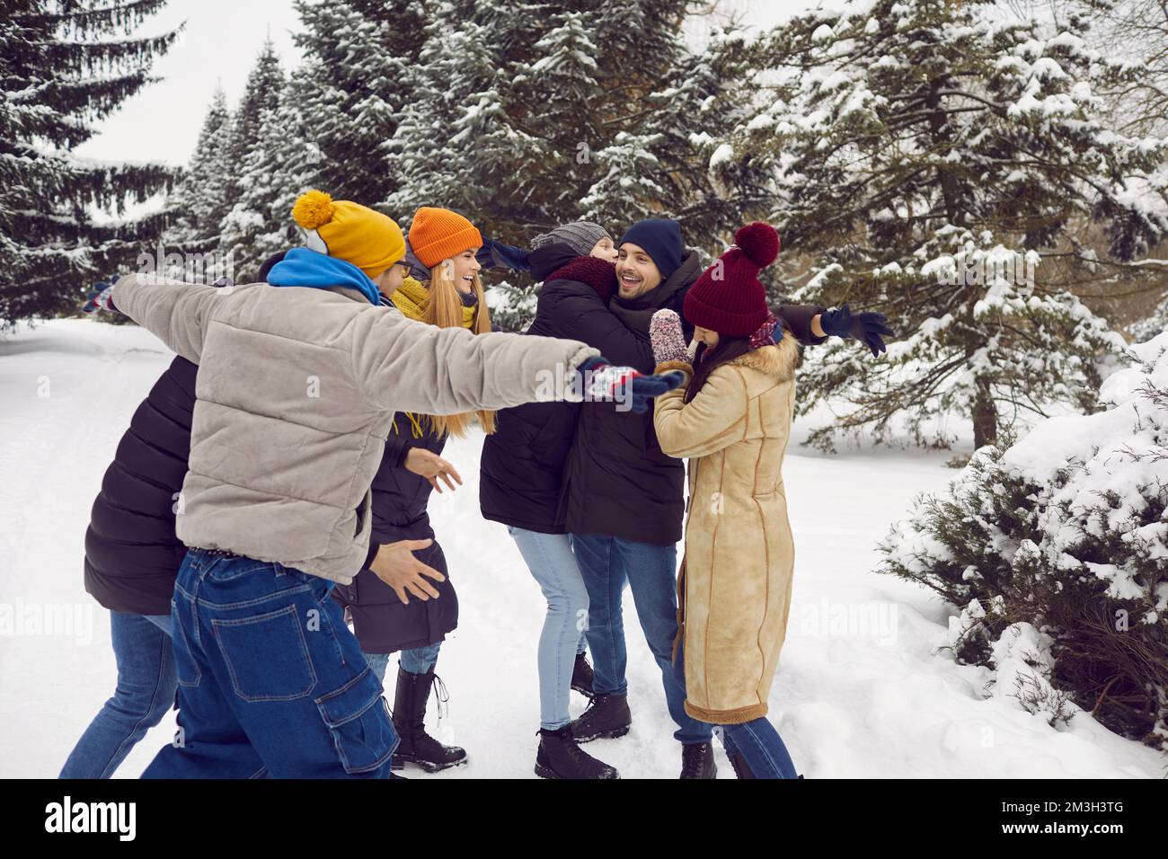 Fröhliche Freunde umarmen und lachen, während sie sich im schneebedeckten Stadtpark oder im Winterwald amüsieren. Stockfoto