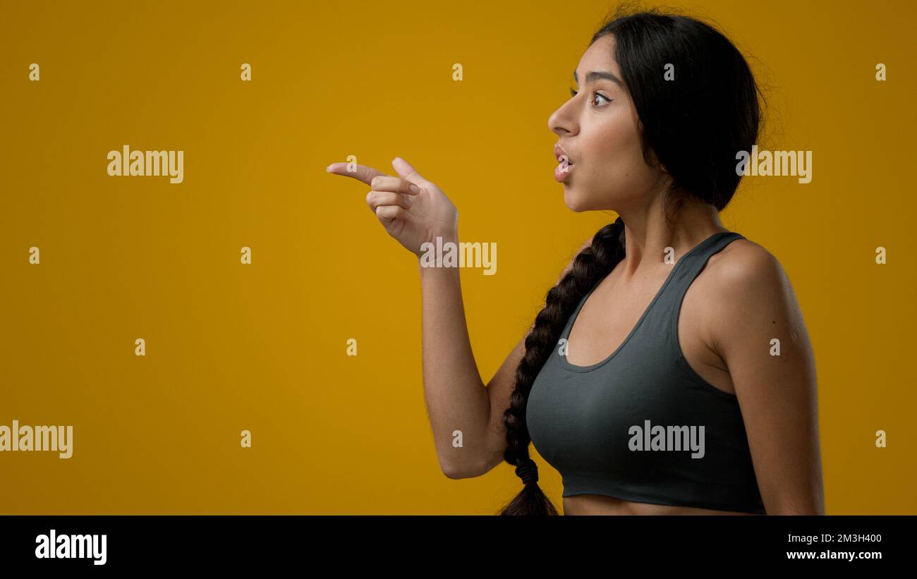 Schockierte, erstaungene, emotionale, indische Frau mit gelbem Studiohintergrund, die auf die Seite zeigt, um leere COPE-Weltraum-Werbung zu zeigen erstaunlich Stockfoto