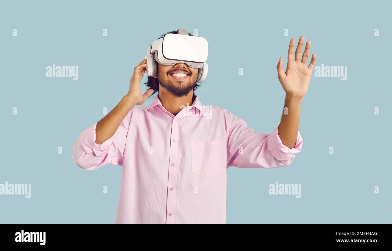 Fröhlicher junger Mann, der Virtual-Reality-Brillen auf pastellfarbenem hellblauem Hintergrund benutzt. Stockfoto