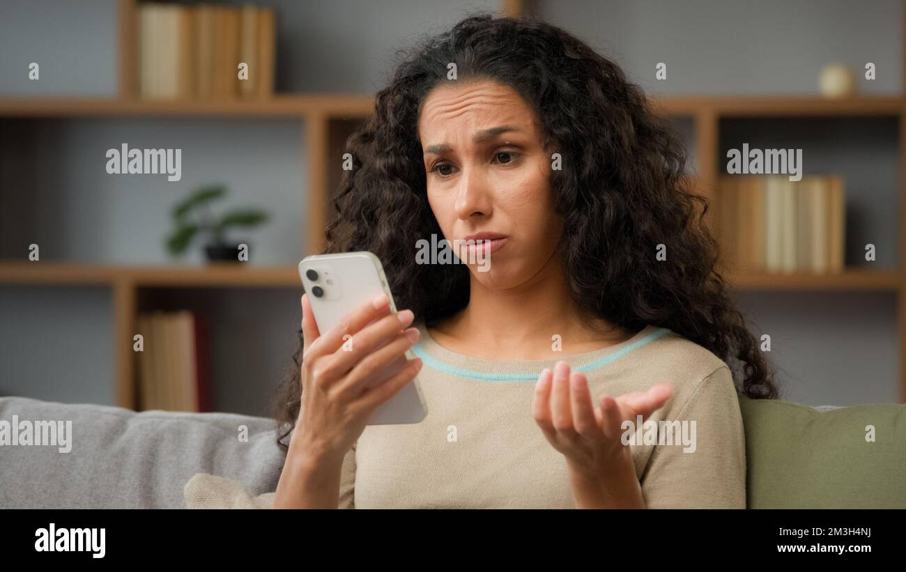 Hispanische traurige unzufriedene Frau hat Problem mit Online-Handy-App unglücklich mit blockiertem Konto in sozialen Netzwerken Blick auf Handy Stockfoto