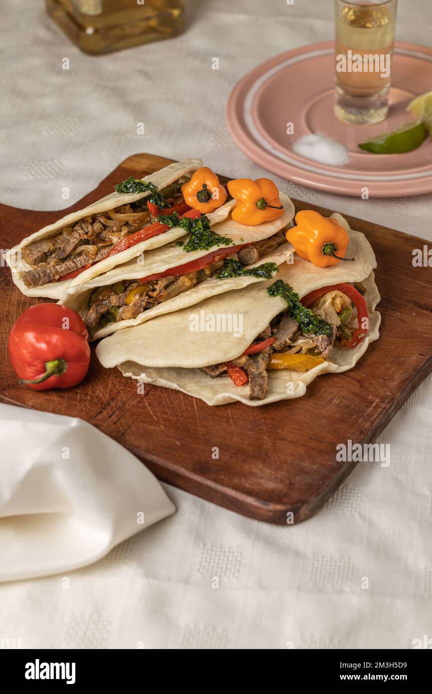 Tacos, typisch mexikanisches Essen, mit Rindfleisch, Gemüse und Gewürzen auf einem Tisch mit weißer Tischdecke. Stockfoto