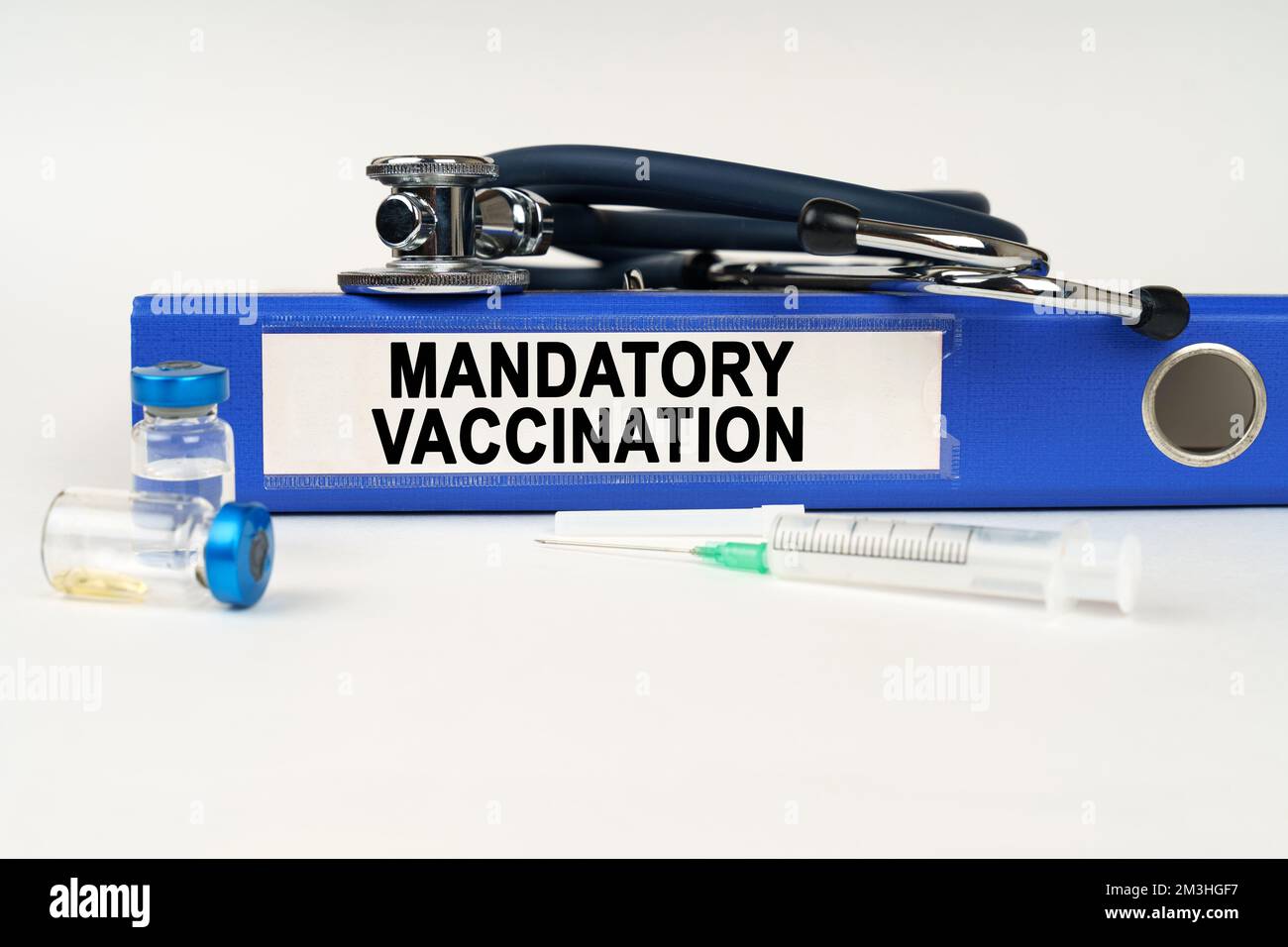 Medizinisches Konzept. Auf einer weißen Oberfläche, einer Spritze, einem Stethoskop und einer Mappe mit der Aufschrift - obligatorische Impfung Stockfoto