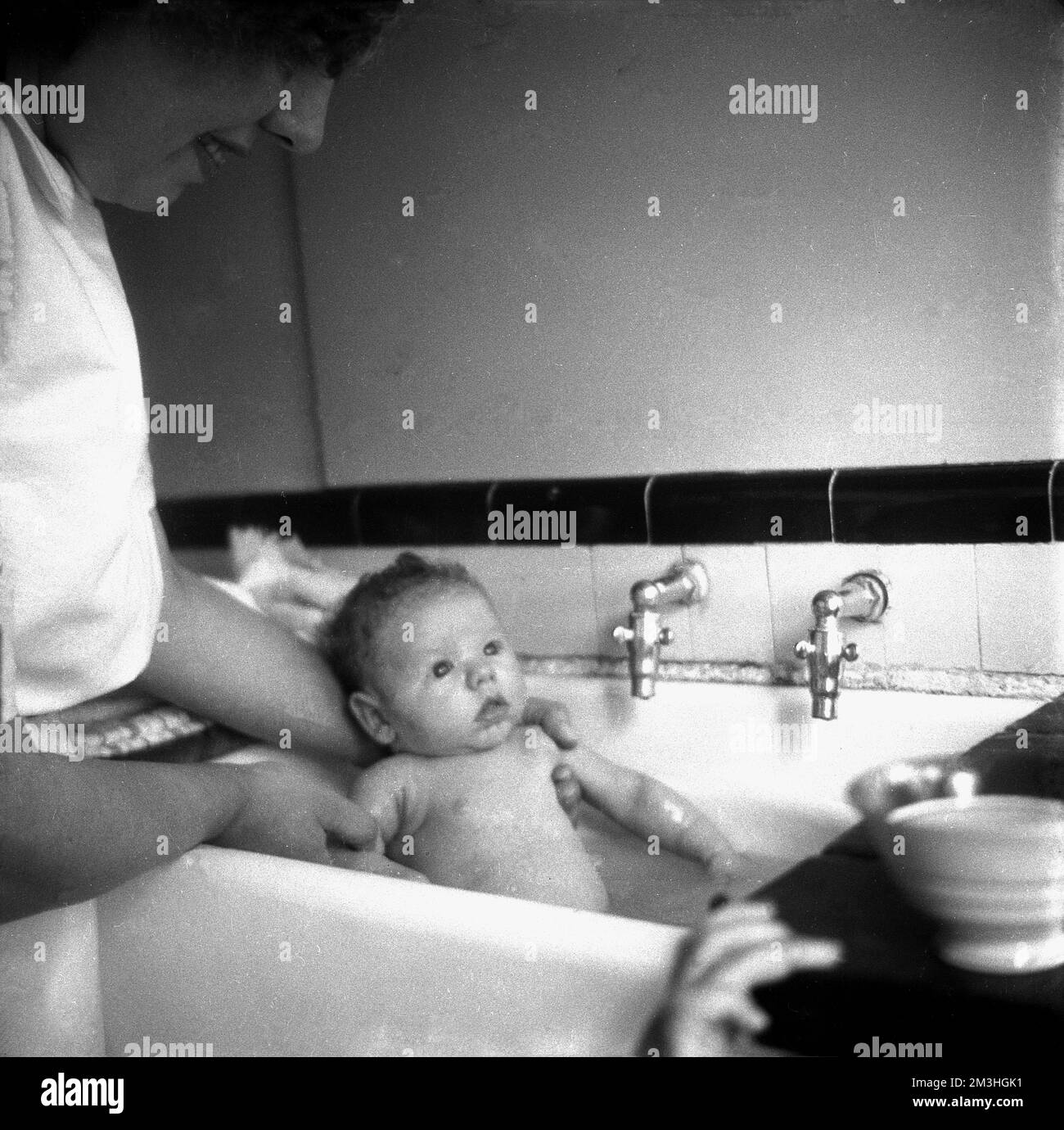 1950er, historisch, eine Mutter, die ihr Baby in einem Keramikwaschbecken badet, England, Großbritannien. Stockfoto