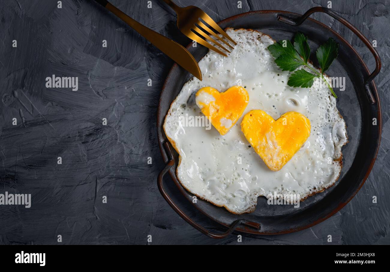 Hausgemachtes Spiegelei in einer Vintage-Pfanne auf grauem Hintergrund. Herzförmiges Eigelb. Stockfoto