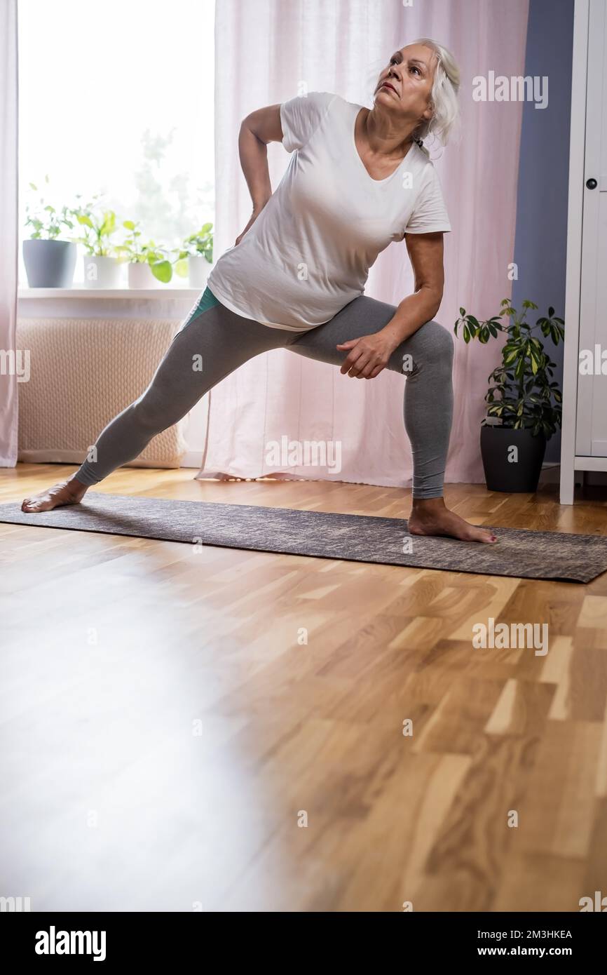Häusliche Yoga-Praxis. Positive, reife Dame in Yoga-Pose Stockfoto
