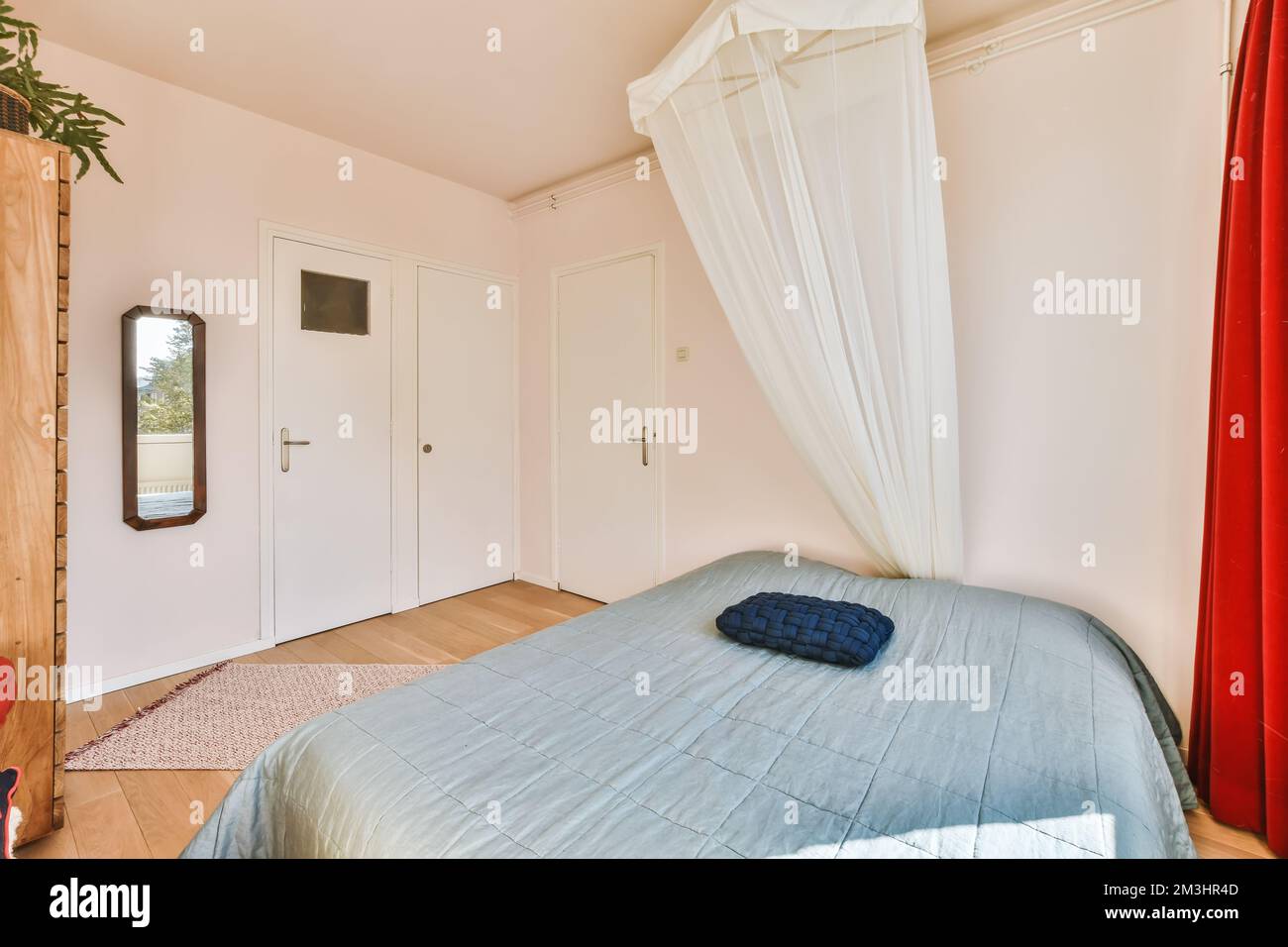 Ein Bett in einem Zimmer mit roten Vorhängen an den Wänden und weißen Vorhängen, die von der Decke darüber hängen Stockfoto