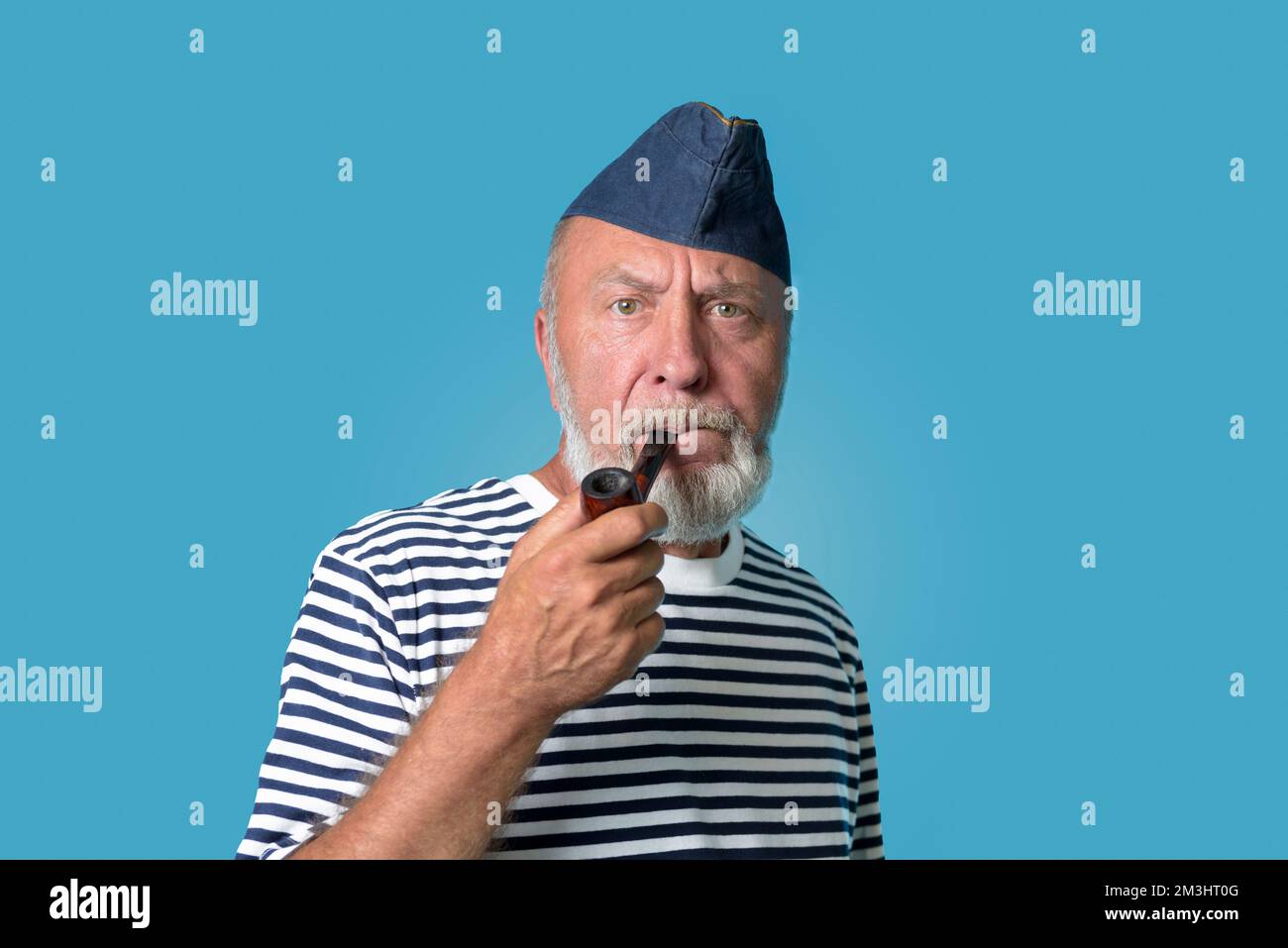 Ein alter Seemann mit einer Rauchpfeife. Porträt eines Seemanns mit blauer Mütze und gestreiftem Hemd in einer marinen Weste. Stockfoto