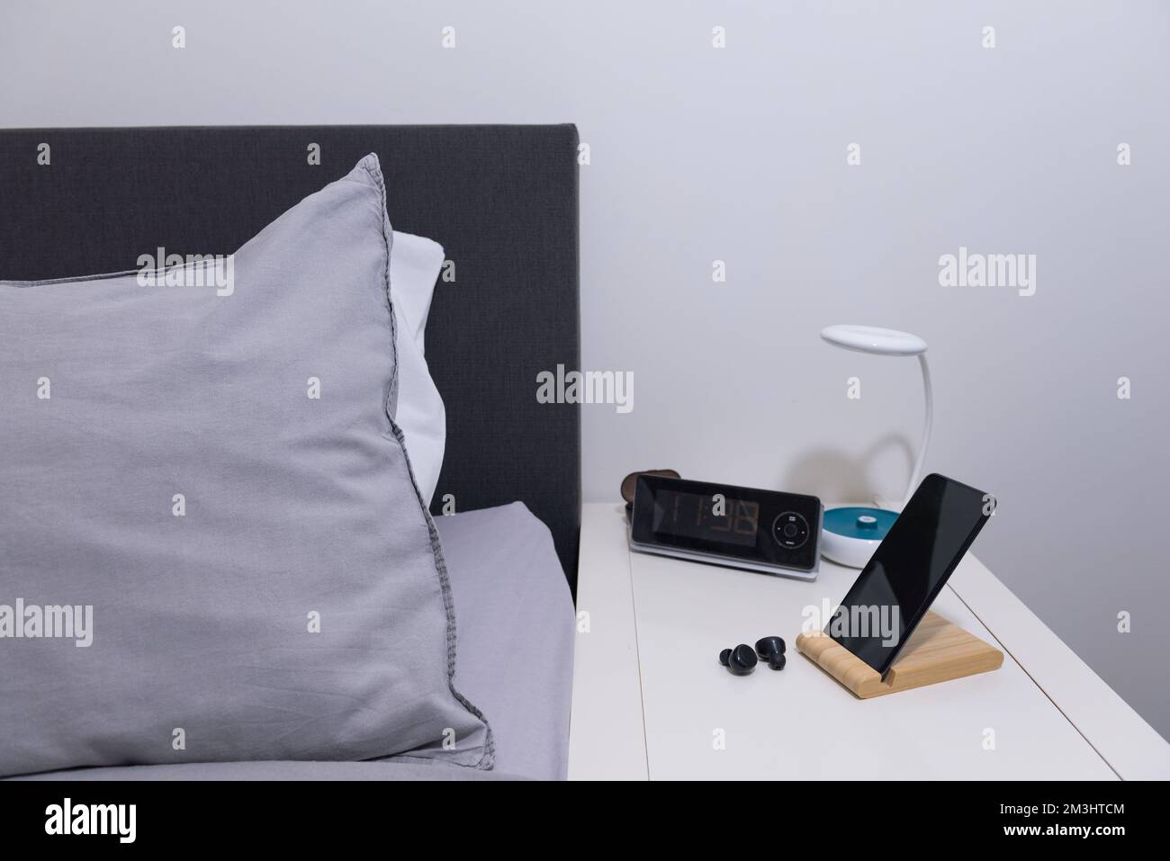 Smartphone auf dem Nachttisch mit Lampe, Headset, Uhr und Bett. Für das Schlafzimmer. Stockfoto
