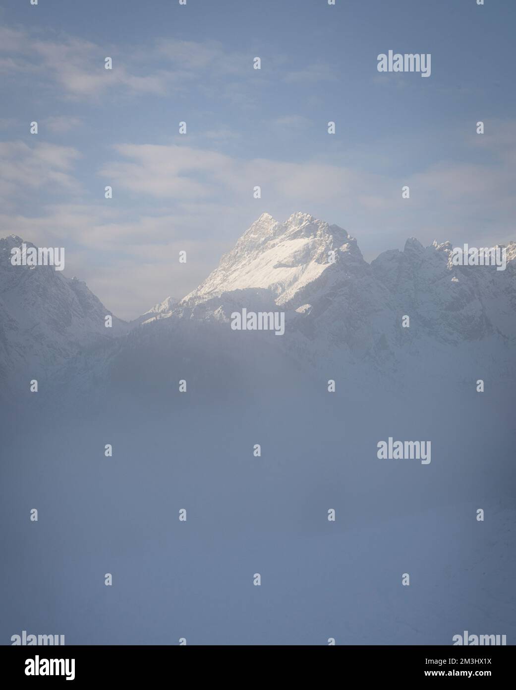 Der schneebedeckte Gipfel eines Berges tritt aus dem Morgennebel in einer alpinen Landschaft hervor Stockfoto