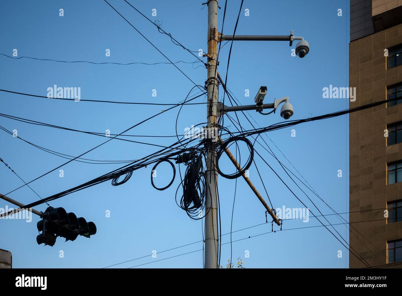 Unordentlicher Pol, blauer Himmel im Hintergrund. Hochspannungsnetz, gefährlich verheddert. Stockfoto