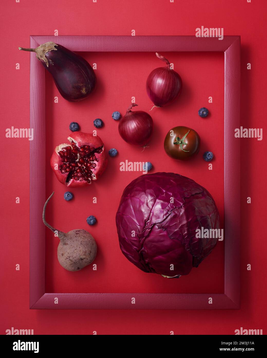 Сabbage, Granatäpfel, Rote Bete, Heidelbeere, Aubergine, Zwiebel und Tomate in Holzbilderrahmen auf rotem Hintergrund Stockfoto