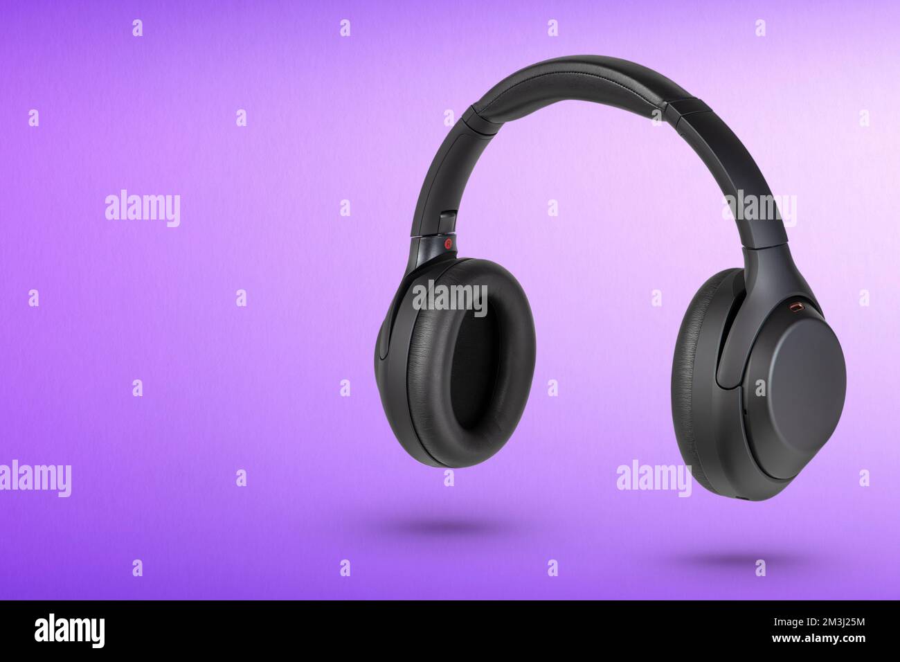 Kopfhörer auf lila Hintergrund. Kabellose Kopfhörer in Schwarz, hohe Qualität, für Werbung oder Produktkatalog. Stockfoto