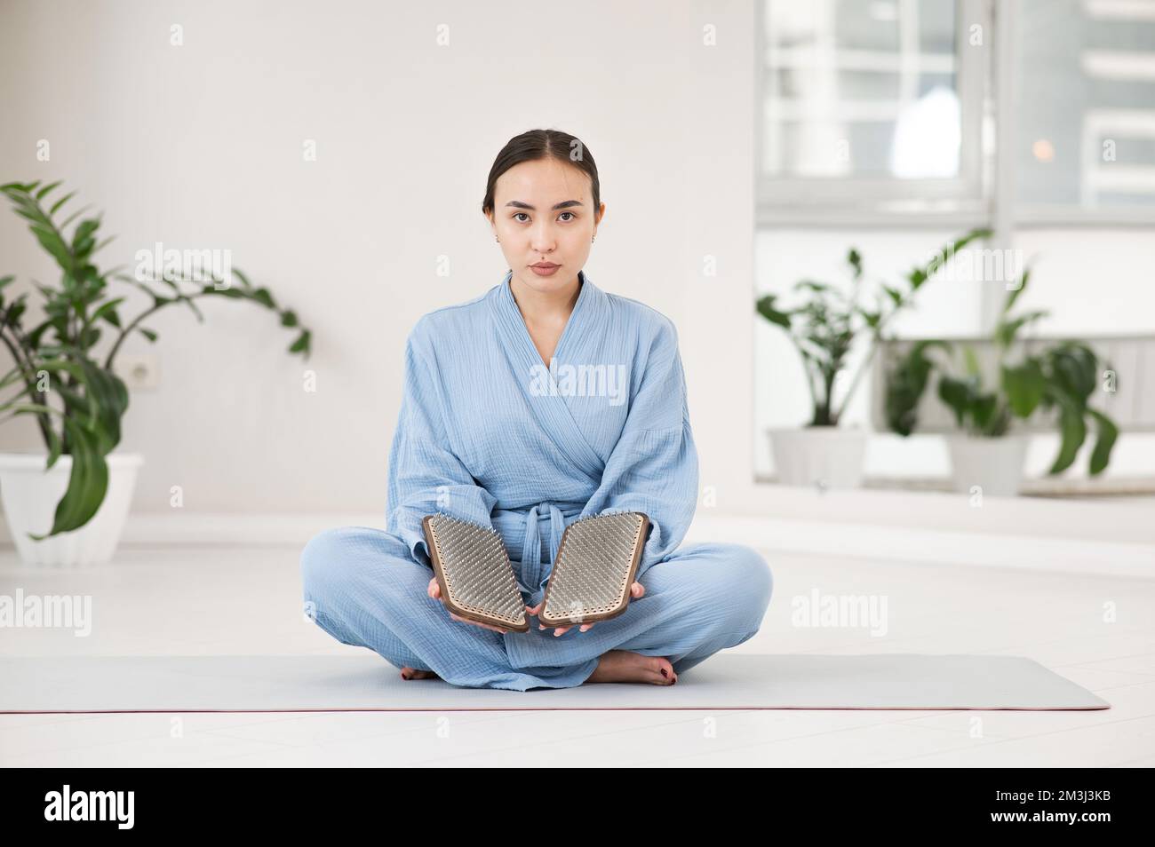 Asiatische Frau sitzt in Lotusposition auf Yogamatte und hält Sadhu-Bretter. Stockfoto