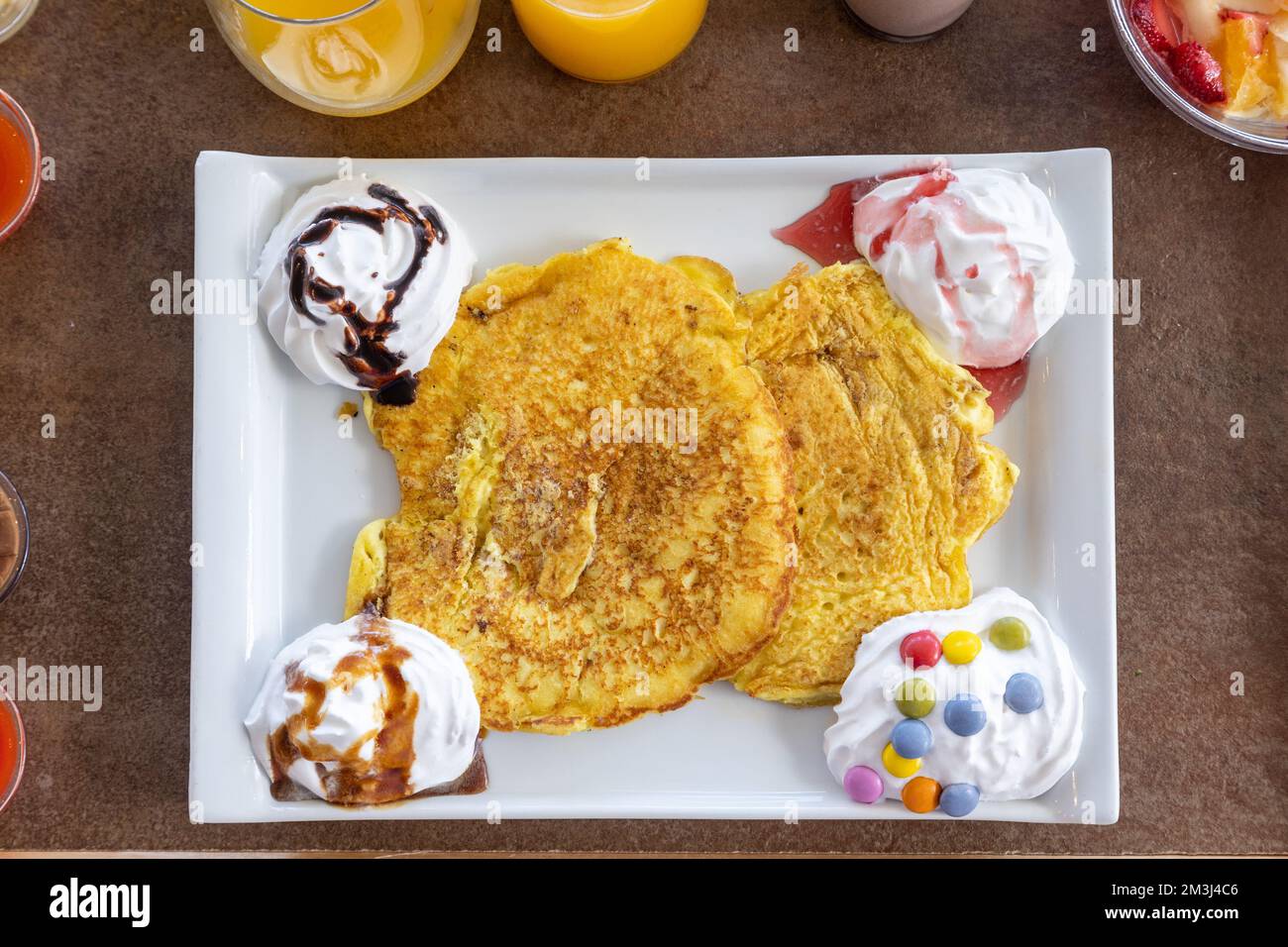 Ein Blick von oben auf einen Pfannkuchen, der mit Schlagsahne und Süßigkeiten auf einem Holztablett serviert wird Stockfoto