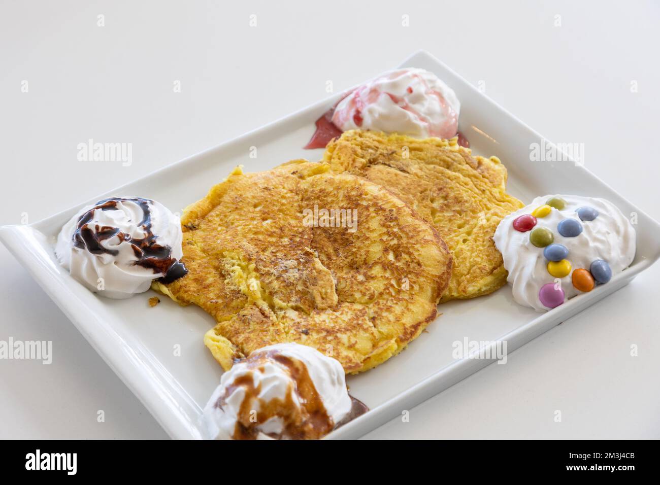 Ein malerischer Blick auf einen Pfannkuchen, der mit Schlagsahne und Süßigkeiten auf einem weißen Tisch serviert wird Stockfoto