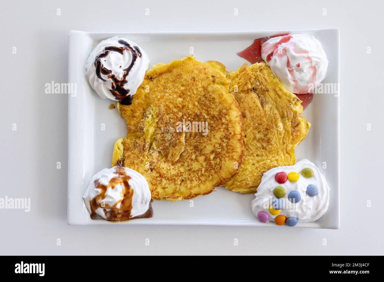 Ein Blick von oben auf einen Pfannkuchen, der mit Schlagsahne und Süßigkeiten auf einem weißen Tisch serviert wird Stockfoto