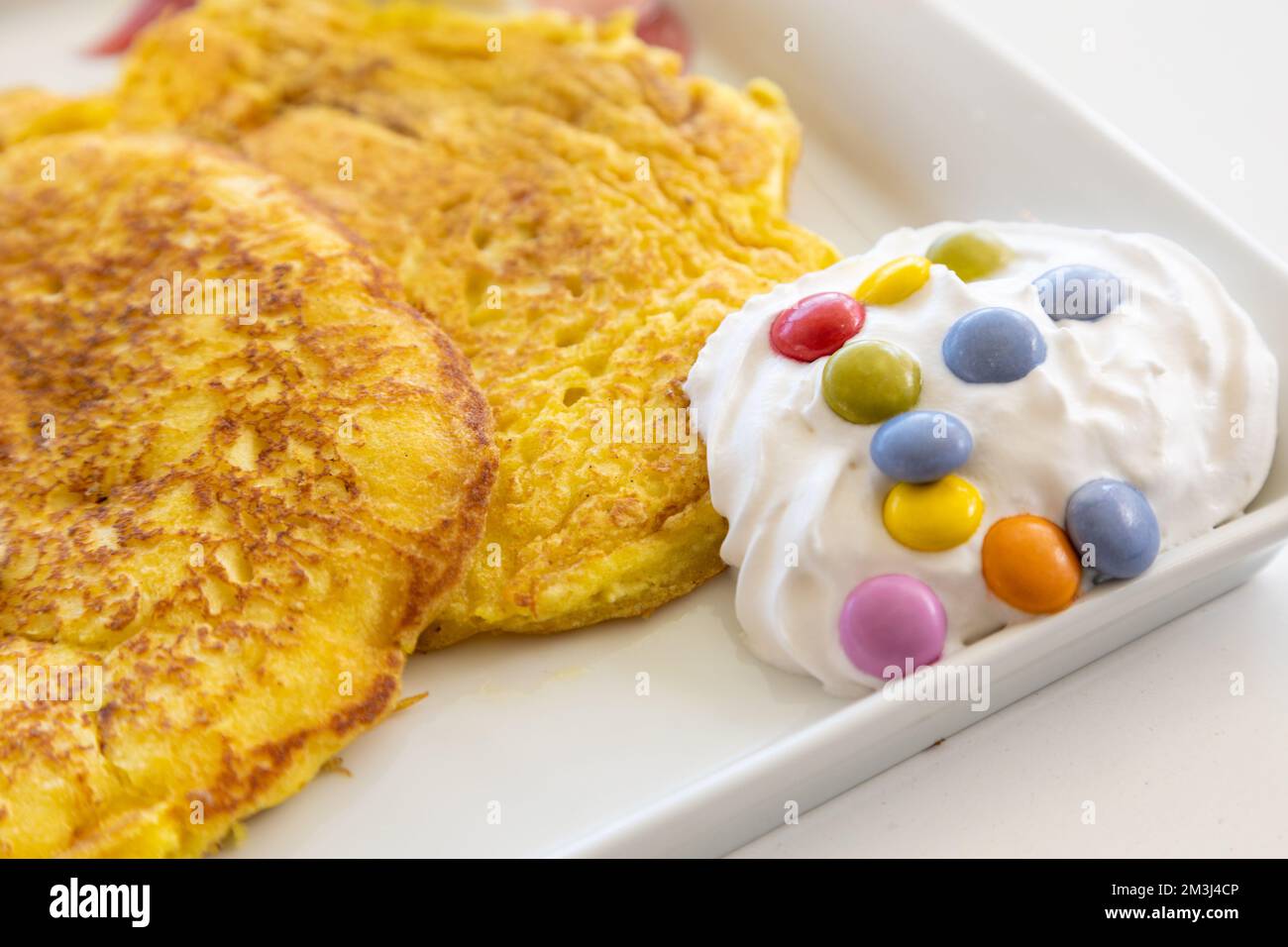 Nahaufnahme eines Pfannkuchen mit Schlagsahne und Süßigkeiten auf einem weißen Tisch Stockfoto