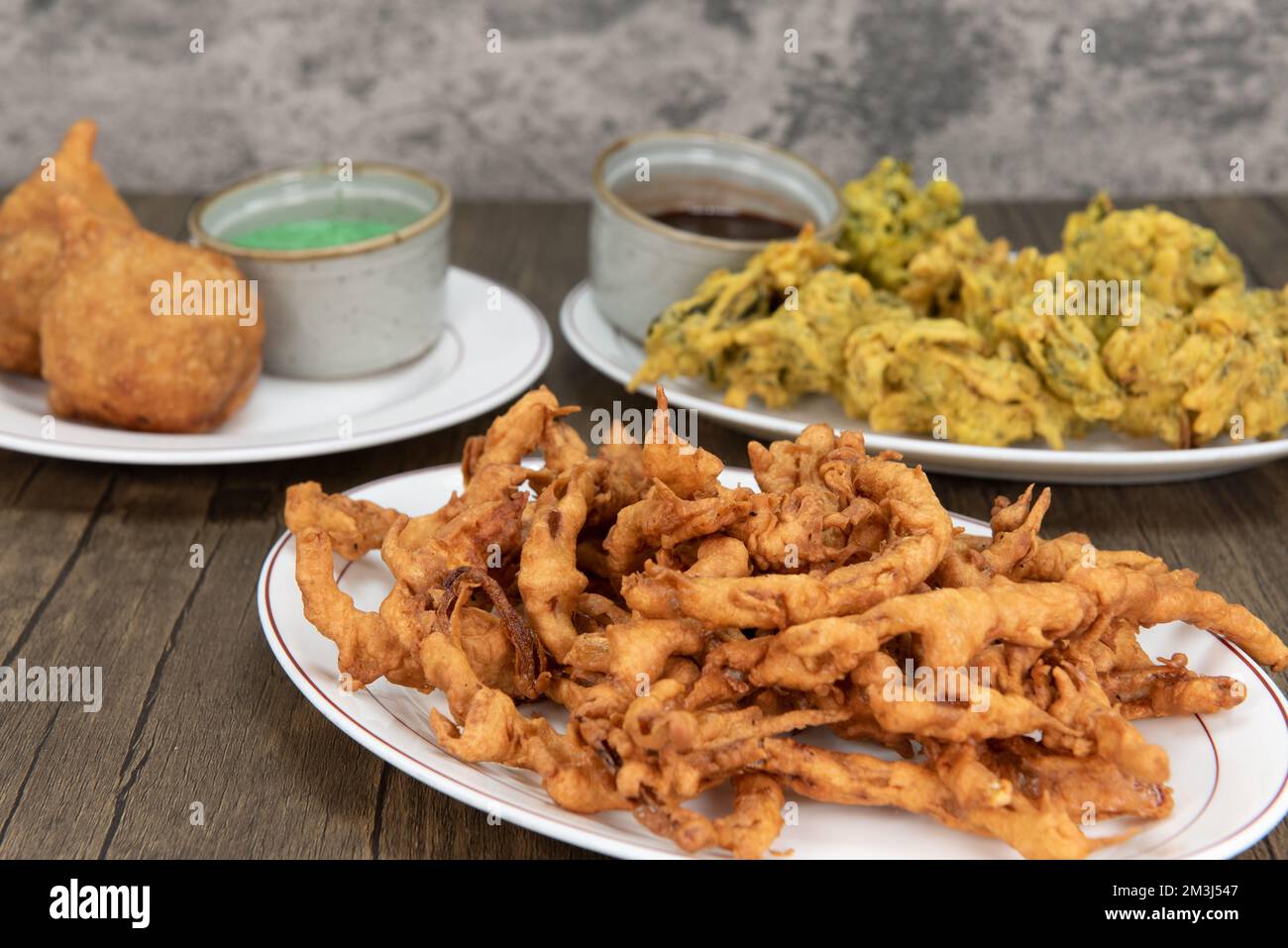 Genießen Sie traditionelle indische Gerichte mit knusprigen Zwiebeln-Bhaji im Vordergrund. Stockfoto