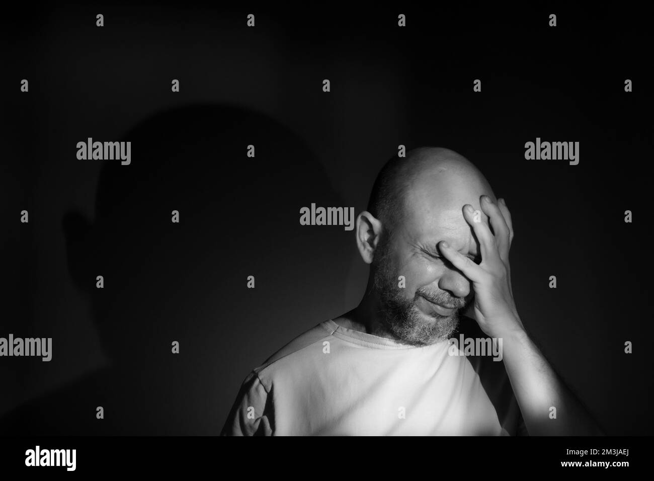 Schwarzweißporträt eines depressiven Mannes mittleren Alters mit Hand-über-Gesicht isoliert auf schwarzem Hintergrund mit finanziellen Problemen oder Loneli-Leiden Stockfoto