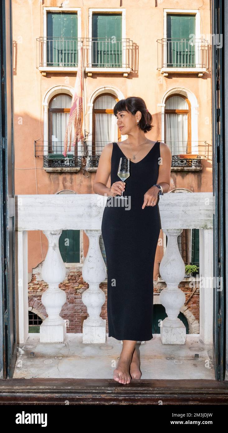 Eine Frau, die ein Glas Sekt auf dem Balkon in Venedig trinkt Stockfoto Eine Frau, die ein Glas Sekt auf dem Balkon in Venedig trinkt Stockfoto