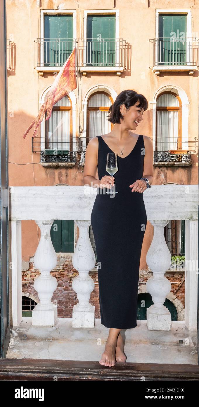 Eine Frau, die ein Glas Sekt auf dem Balkon in Venedig trinkt Stockfoto Eine Frau, die ein Glas Sekt auf dem Balkon in Venedig trinkt Stockfoto