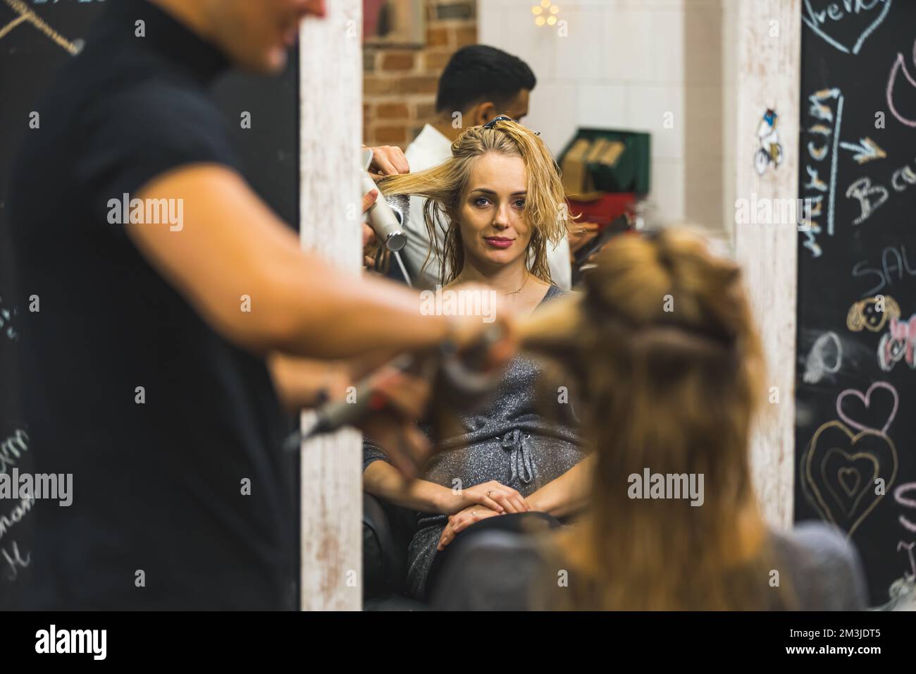 Rückspiegelansicht eines männlichen Friseurs, der lange nasse Haare einer Frau trocknet. Hochwertiges Foto Stockfoto