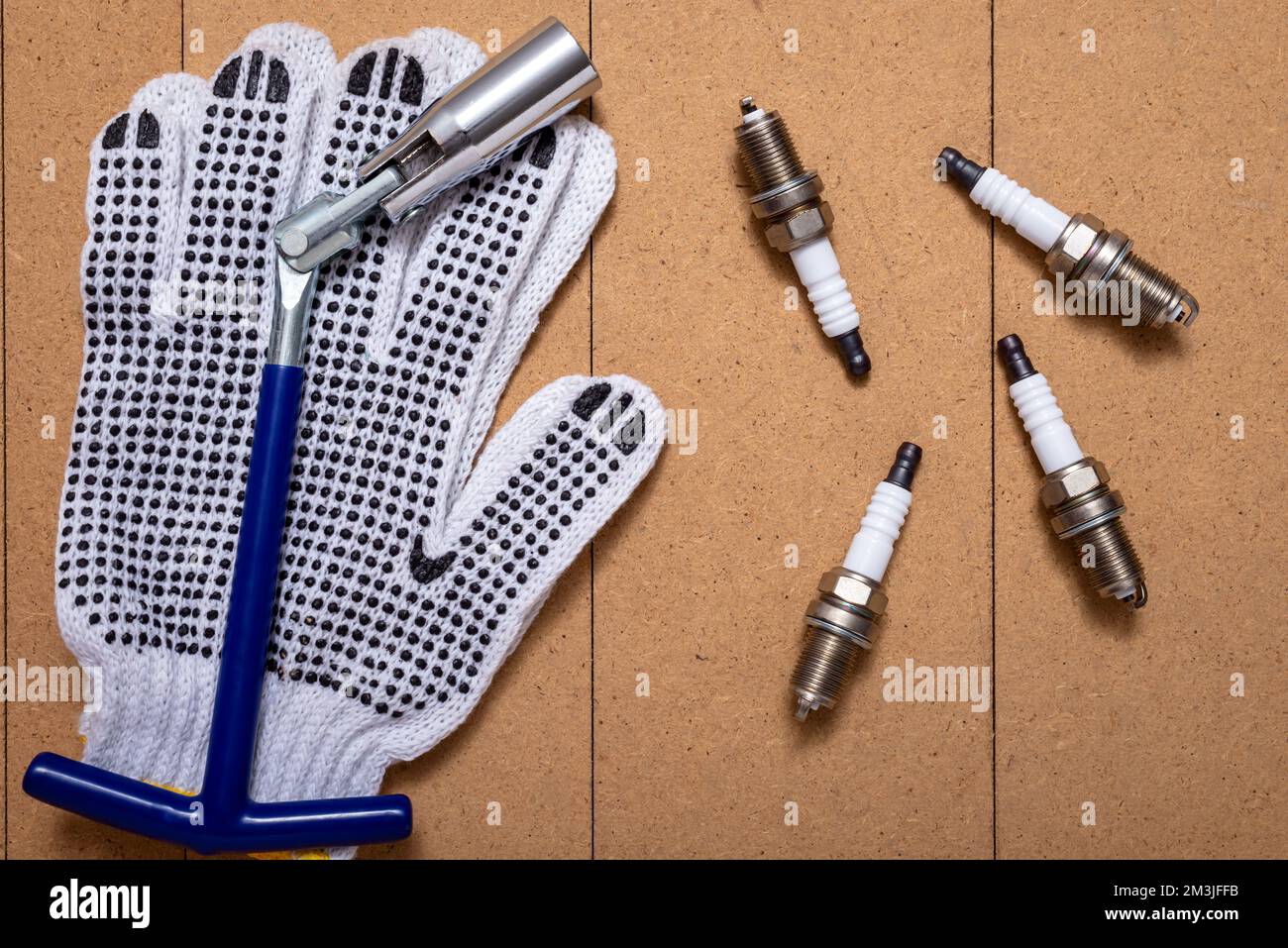 Zündkerzen, Zündkerzenschlüssel und Schutzhandschuhe auf Holztisch. Stockfoto