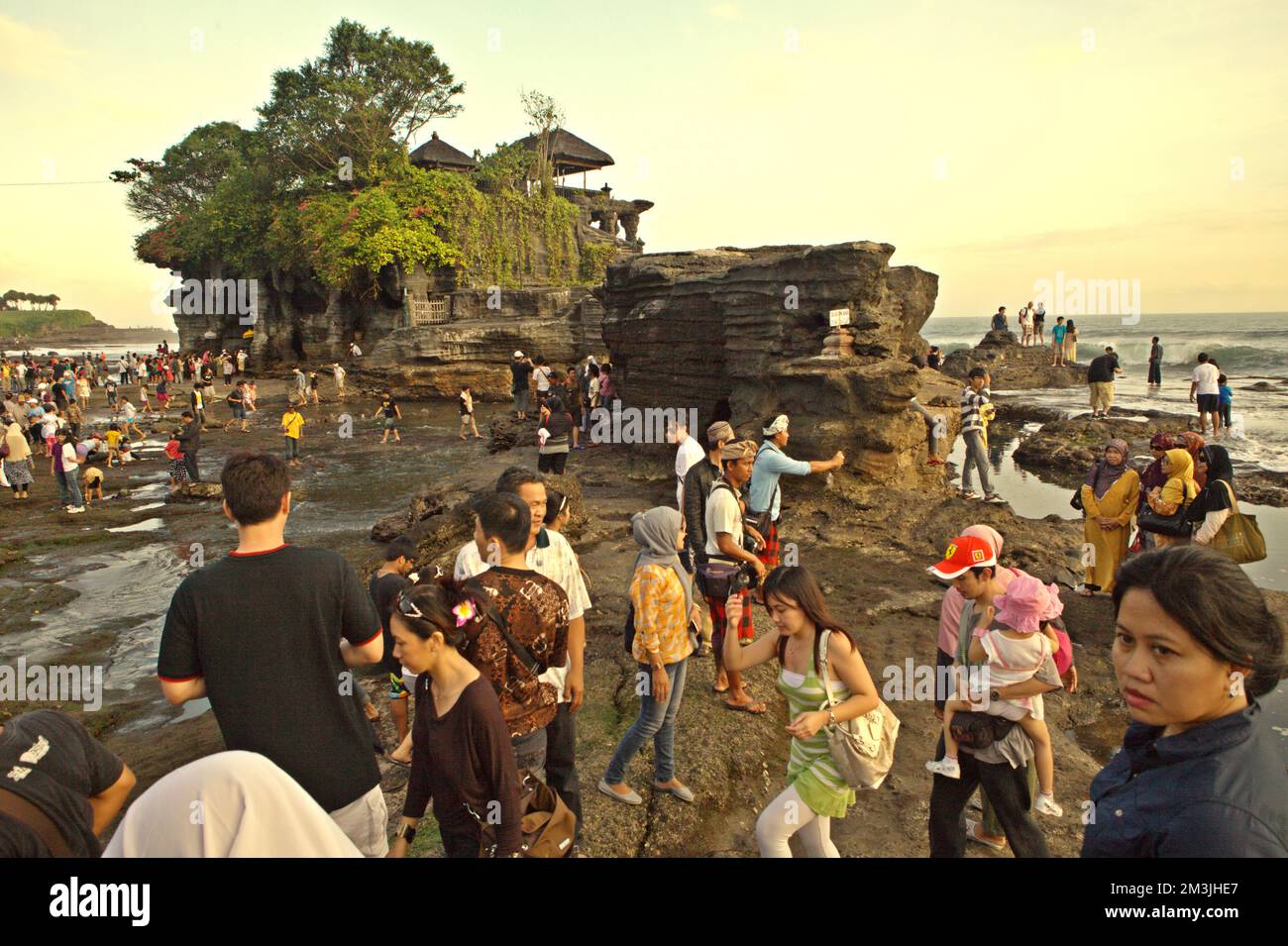 Touristen haben Zeit zur freien Verfügung an einem felsigen Strand, im Hintergrund einer Klippe, wo Pura Tanah Lot, ein bekannter hinduistischer Tempel und kulturelles Symbol für Reisefotografie, in Tabanan, Bali, Indonesien. "Religiöse Stätten werden nicht nur von den Pilgern besucht, sondern auch von nichtreligiösen Touristen, da sie kulturelle, historische und religiöse Bedeutung haben. Der religiöse Tourismus ist weniger von diesen wirtschaftlichen Problemen betroffen, da der Grund für Reisen sehr stark ist und eine sehr wichtige Rolle in ihrem Leben (den Touristen) spielt, so dass Geld keine sehr wichtige Rolle spielt Stockfoto