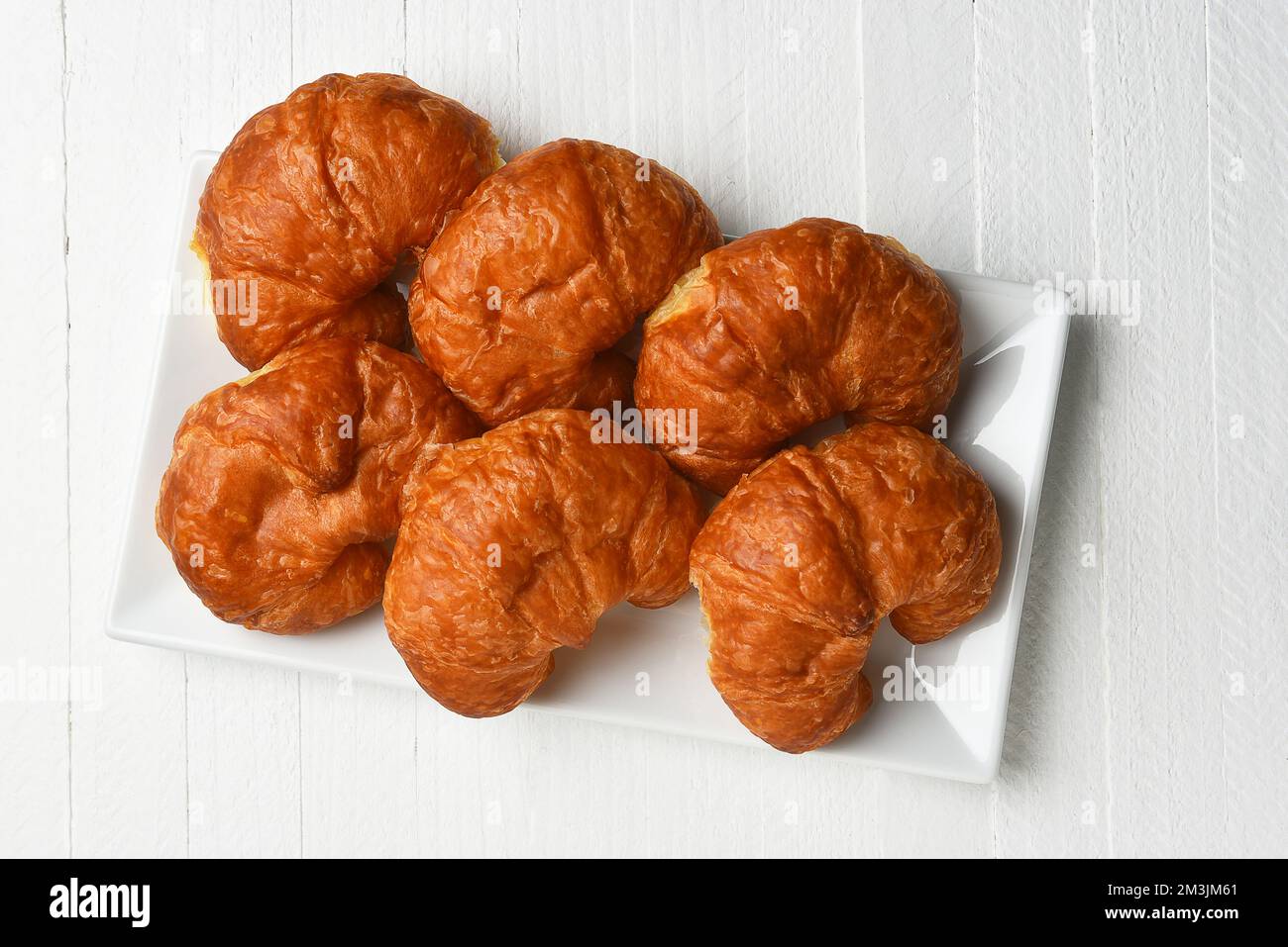 Sechs Croissants aus einem hohen Winkel auf einer weißen Platte auf einem rustikalen weißen Holztisch. Stockfoto