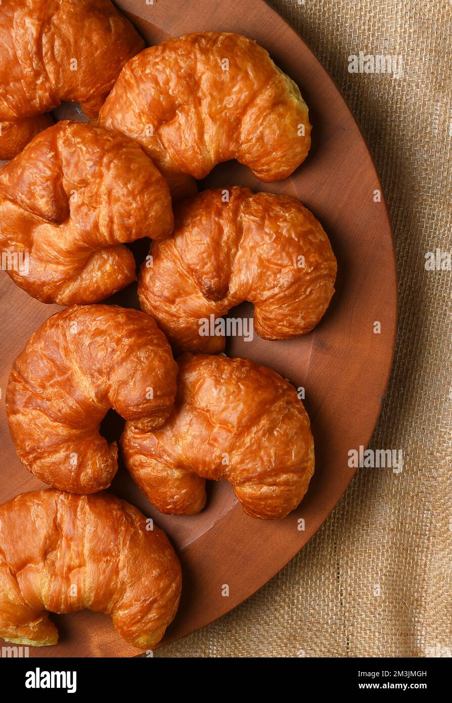 Frisch gebackene Croissants auf einer Holzplatte und einem Latztischtuch. Stockfoto