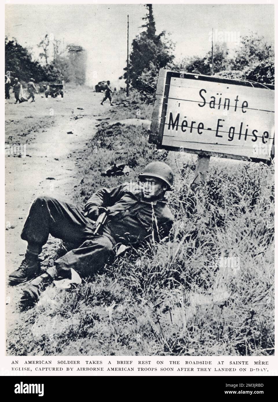 Ein amerikanischer Fallschirmjäger ruht sich kurz am Straßenrand in St. Nur Eglise, Normandie. Diese Stadt wurde von amerikanischen Luftwaffenleuten eingenommen, kurz nachdem sie am D-Day, dem 6. Juni 1944, gelandet waren. Stockfoto