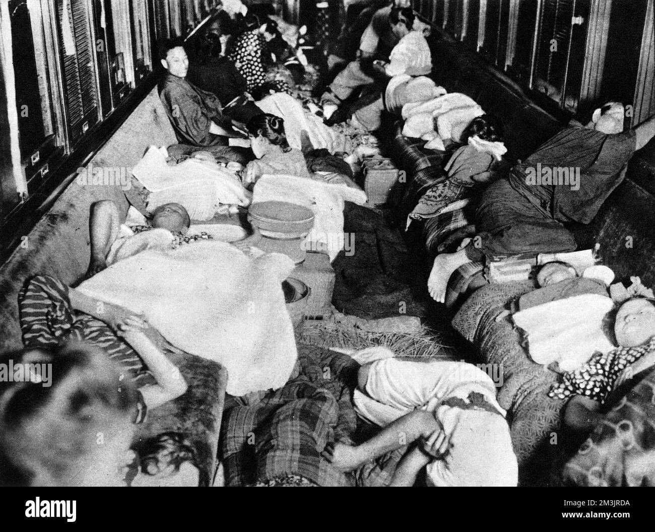 Ein Eisenbahnbunker für die Nacht, in dem Männer, Frauen und Kinder in einer Kutsche auf einem Nebengleis am Bahnhof Numadzu zusammenkamen, nach dem katastrophalen Erdbeben, von dem Tokio und die Nachbarstadt Yokohama im Jahr 1923 heimgesucht wurden. Das Erdbeben ereignete sich am 1.. September mittags, zu einer Zeit, als viele Menschen ihre Mahlzeiten zubereiteten. Die Brände breiteten sich aus und zerstörten alles, was das Erdbeben hinterlassen hatte. Die Zahl der Todesopfer stieg auf über 70000, und viele weitere Menschen blieben obdachlos. Datum: 1923 Stockfoto