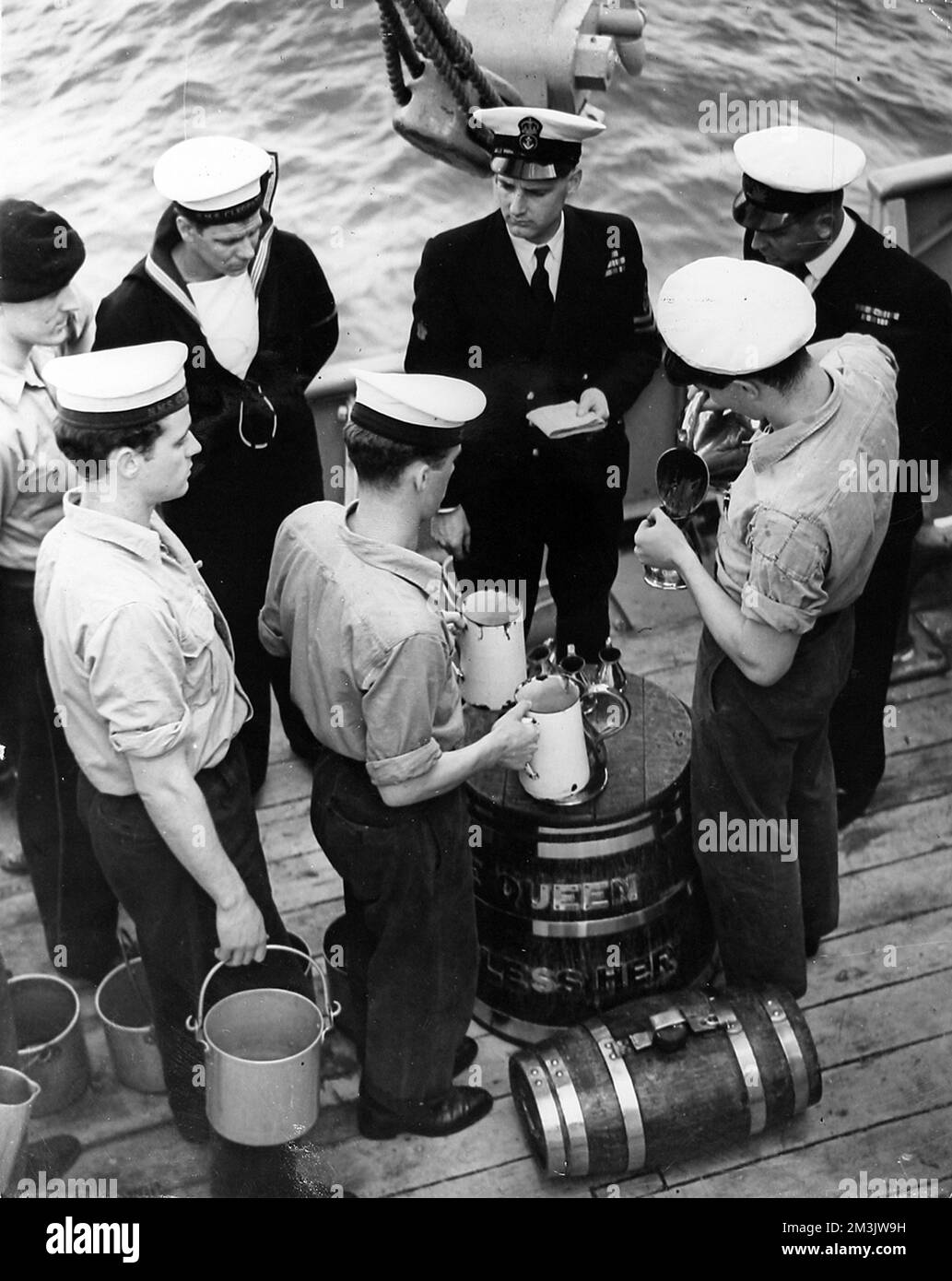 Das Foto zeigt die Verteilung von Rum auf die Quoten an Bord von HMS „Cleopatra“ nach Königin Elizabeth II. Erster Bestellung – „Aufsplittern der Hauptstütze“ – nach ihrer Überprüfung der Flotte. Wie sich zeigt, beobachten mehrere Beamte die Verfahren, um die ordnungsgemäße Zuweisung sicherzustellen. Datum: 1953 Stockfoto