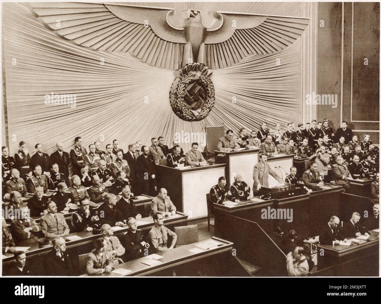 Adolf Hitler auf der 1. Tagung des Großen Deutschen Reichstags in der Kroll-Oper, Berlin, 30. Januar 1939. Der riesige Adler im Hintergrund ist repräsentativ für die Kontrolle des Reichstags durch die Nazis und die Macht des „Führers“ Adolf Hitler. Stockfoto