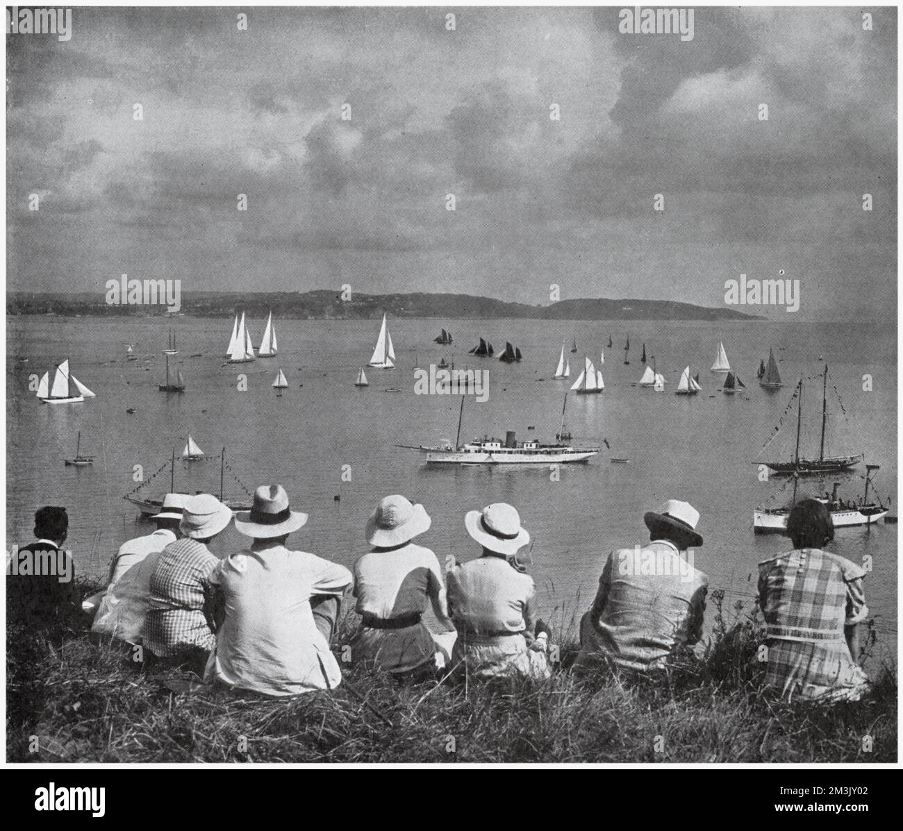 Eine Gruppe von Urlaubern, die die Brixham Regatta von einem Aussichtspunkt auf einer Klippe im West Country, 1936, beobachten. Eine Reihe von Fischtrawlern mit dunklen Segeln teilen sich die Gewässer mit den weißen Segeln der Rennyachten. Stockfoto