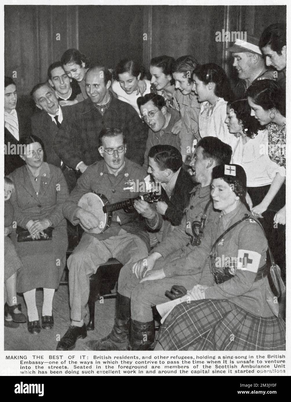 Ein "Sing-Song" in der britischen Botschaft in Madrid, während der frühen Phasen des Spanischen Bürgerkriegs 1936. Eine Reihe britischer Bürger in Madrid hatte in der Botschaft Zuflucht gesucht, und dies war eine der Möglichkeiten, wie sie die Zeit vergingen, während sie sich vor dem Krieg draußen versteckten. Im Vordergrund steht eines der Mitglieder der schottischen Ambulanzeinheit. Stockfoto