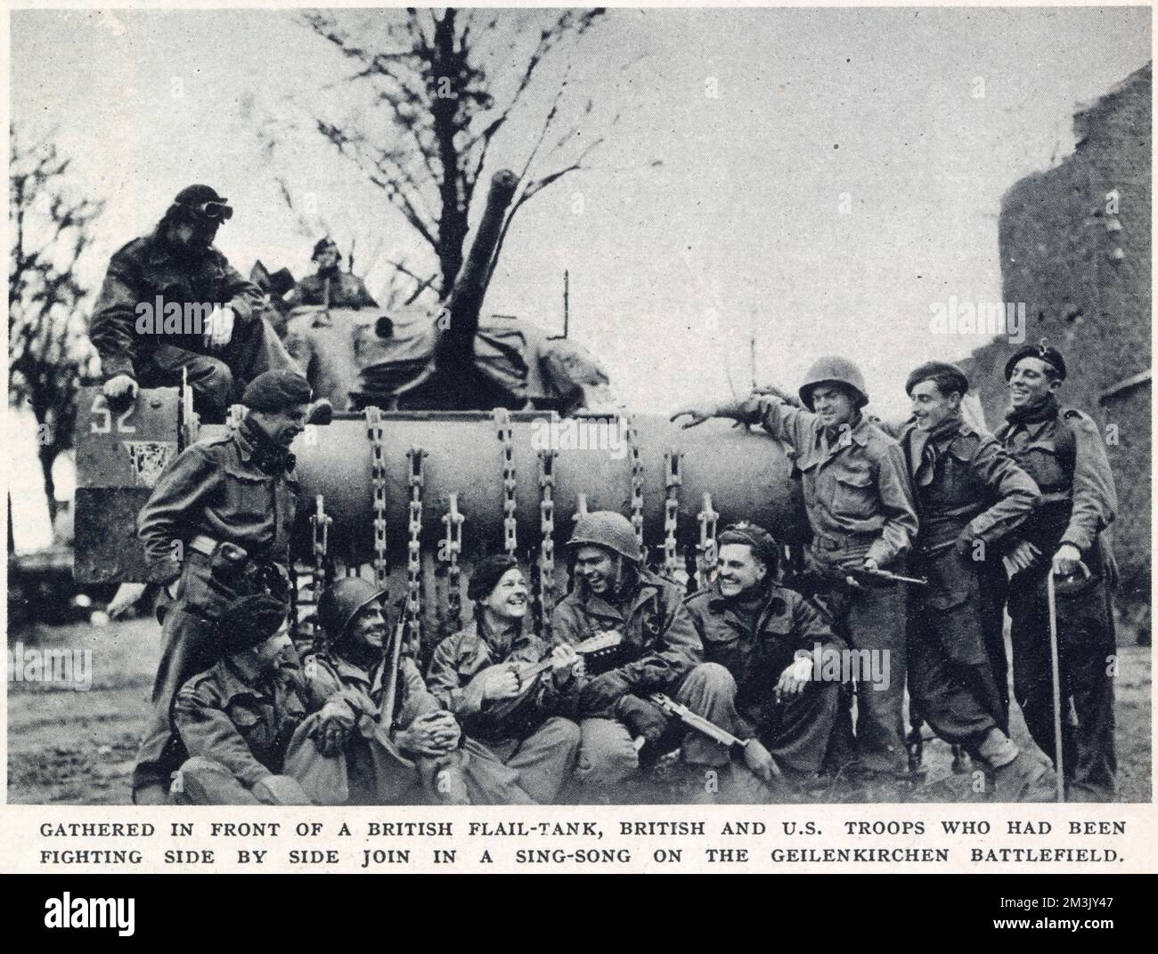 Britische und amerikanische Truppen, die Ende 1944 vor einem Sherman-Flail-Panzer in der Nähe von Geilenkirchen ein Lied singen. Geilenkirchen war ein Schlüsselpunkt der deutschen „Siegfried-Linie“ und wurde im November 1944 von einer kombinierten Truppe britischer und amerikanischer Soldaten gefangen genommen. Stockfoto