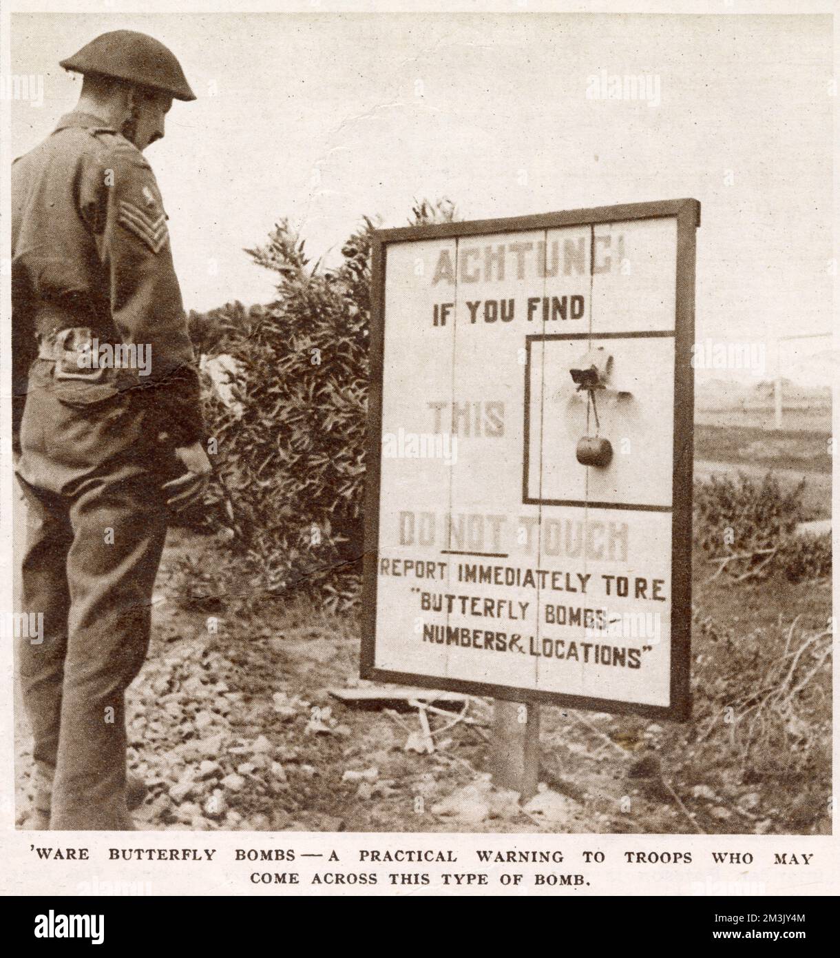 Ein britischer feldwebel, der auf eine Warnmeldung zu den Antipersonenminen "Schmetterling" in Italien während des Zweiten Weltkriegs schaut. Die Warnung weist jeden, der eine dieser Bomben findet, an, sie nicht zu berühren und sie den königlichen Ingenieuren zu melden. Stockfoto