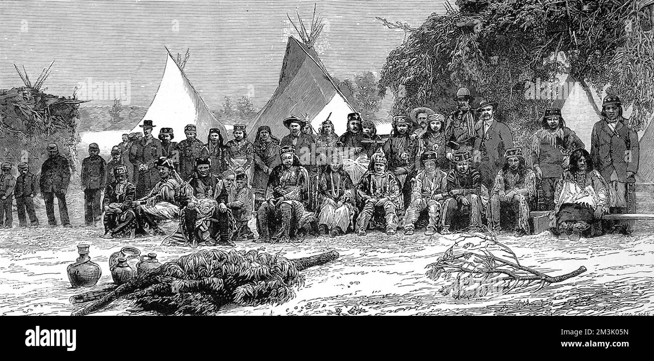 Große Gruppe von Apachen-Indianern in einer Mischung aus einheimischer und europäischer Kleidung, mit Wigwams im Hintergrund. Datum: 1884 Stockfoto