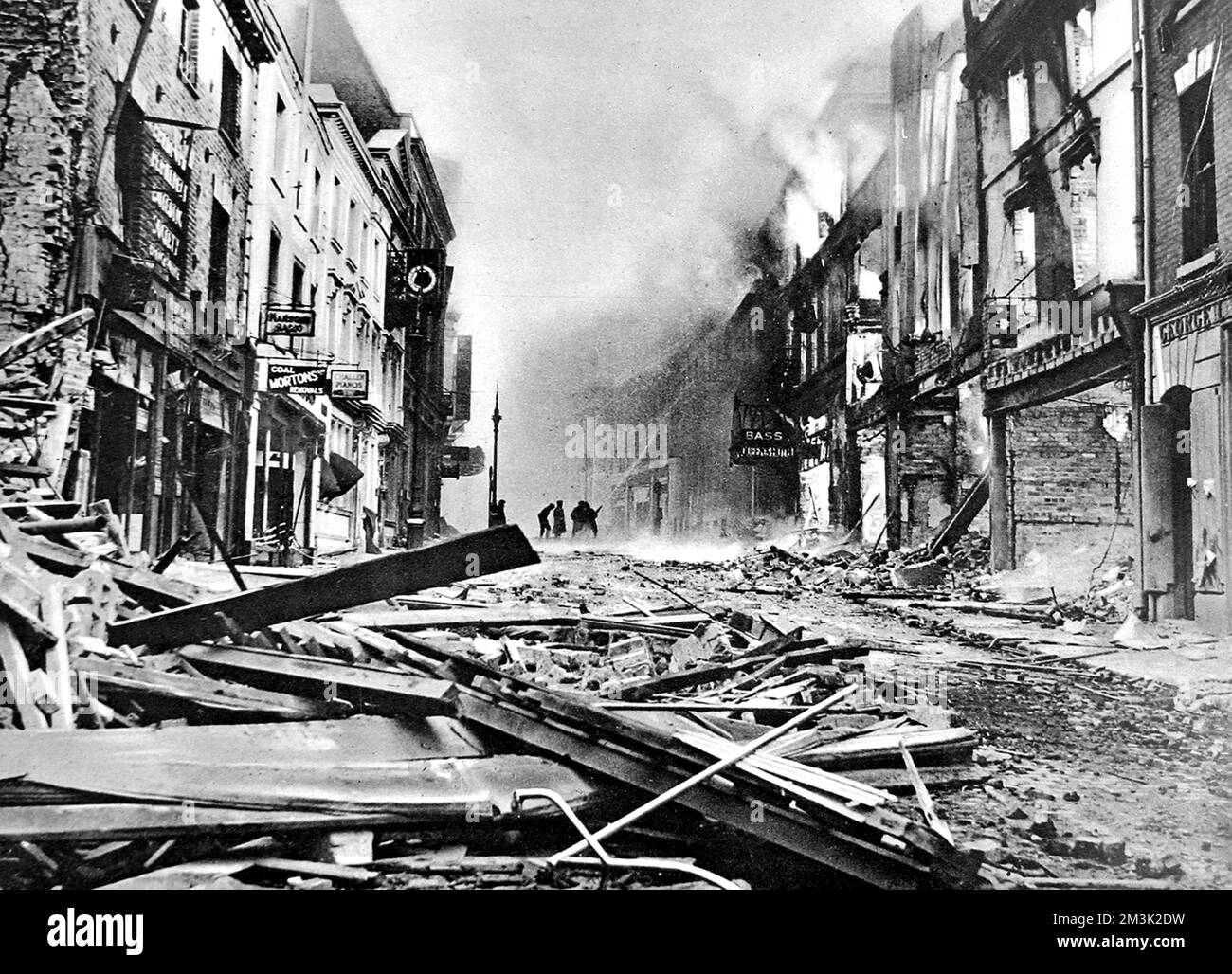 Eine der Hauptstraßen von Coventry, brennt noch nach einem deutschen Luftangriff, 1940. Im Hintergrund pumpt eine Gruppe von Feuerwehrleuten Wasser auf einen der Flammen. Datum: November 1940 Stockfoto